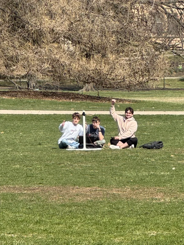 Three team members outdoors beside ground-station equipment during testing.